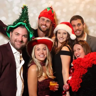Friends in Santa hats and holiday props at a holiday party photo booth