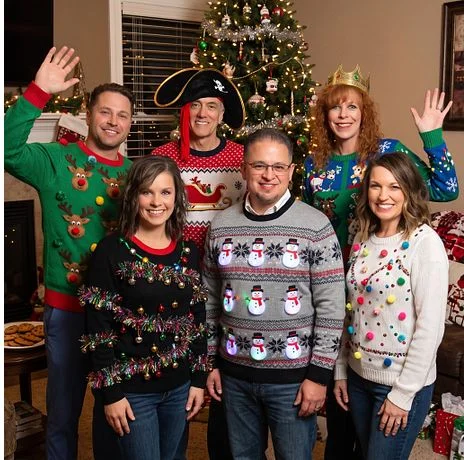 A group in ugly holiday sweaters by a tree