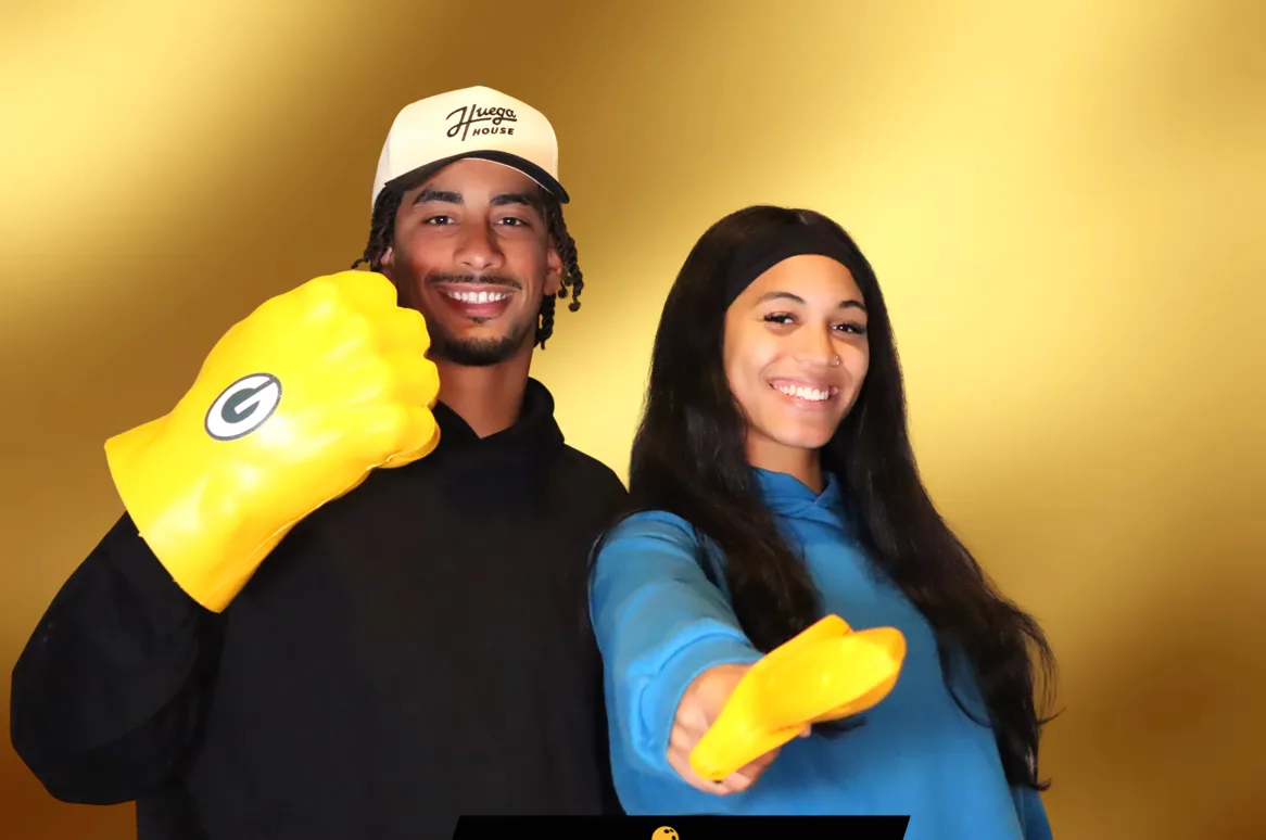 Two fans with foam fingers posing with a football player at a charity event