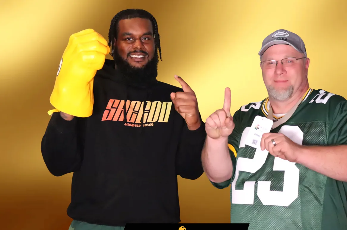 A fan in a jersey posing with a football player against a gold backdrop